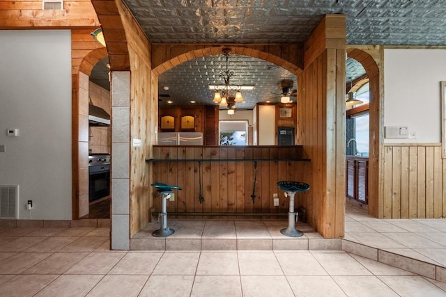 kitchen with visible vents, black oven, wood walls, wainscoting, and tile patterned floors