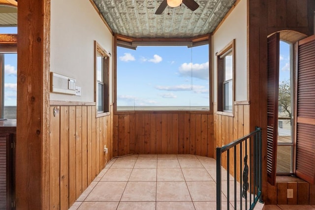 corridor with light tile patterned floors, wooden walls, arched walkways, and a wainscoted wall