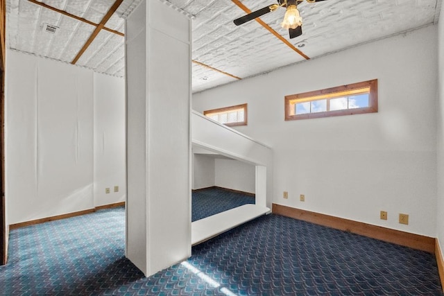 interior space featuring baseboards, visible vents, a ceiling fan, and carpet