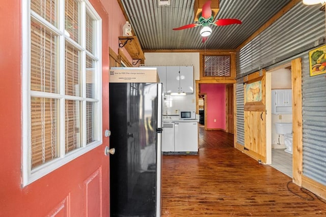 kitchen with wood finished floors, white microwave, a ceiling fan, freestanding refrigerator, and white cabinetry