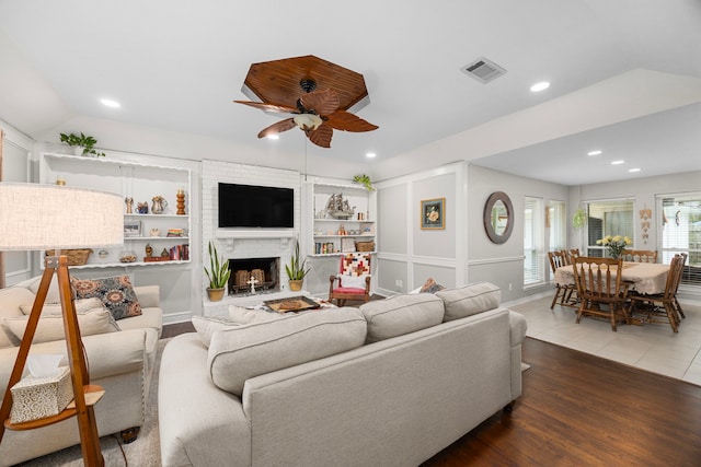 living area with visible vents, a brick fireplace, ceiling fan, lofted ceiling, and wood finished floors