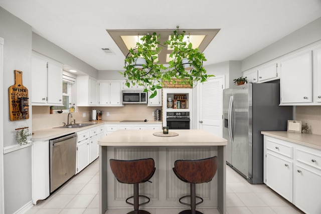 kitchen featuring a kitchen island, a sink, black appliances, white cabinets, and a kitchen breakfast bar