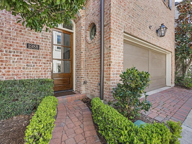 view of exterior entry featuring brick siding, decorative driveway, and a garage