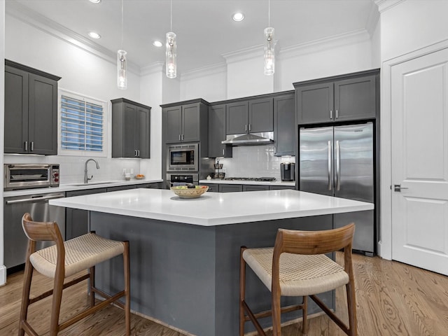 kitchen with a breakfast bar area, light wood finished floors, a sink, under cabinet range hood, and appliances with stainless steel finishes