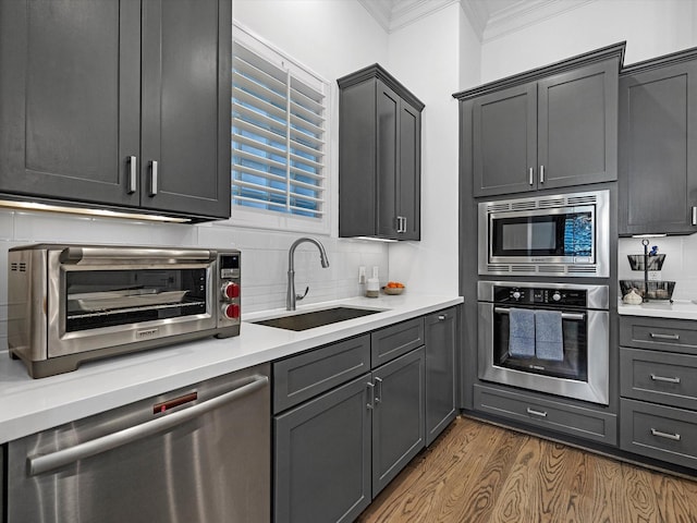 kitchen featuring ornamental molding, a sink, tasteful backsplash, wood finished floors, and appliances with stainless steel finishes