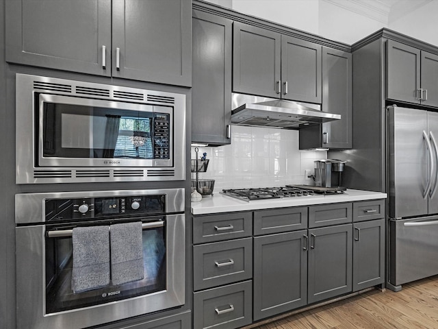 kitchen with tasteful backsplash, under cabinet range hood, light countertops, light wood-style flooring, and appliances with stainless steel finishes