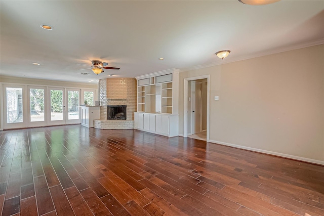 unfurnished living room with a brick fireplace, dark wood finished floors, a ceiling fan, and crown molding