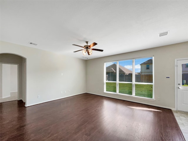 empty room with a ceiling fan, wood finished floors, visible vents, and arched walkways