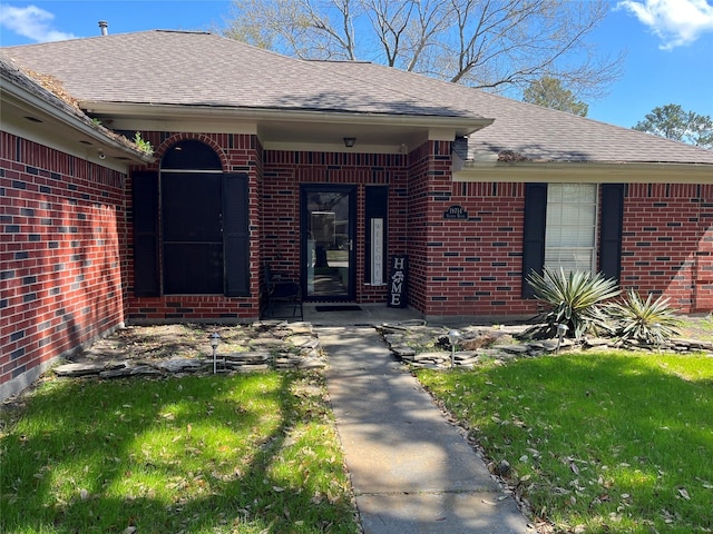 entrance to property with brick siding, a shingled roof, and a yard