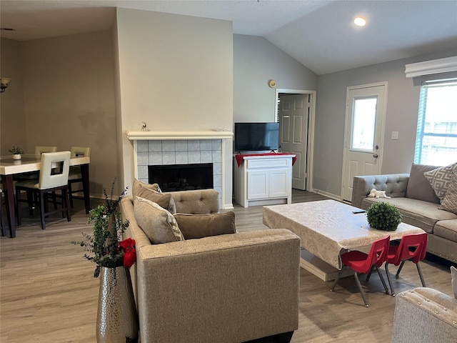 living area featuring light wood finished floors, baseboards, lofted ceiling, and a tile fireplace