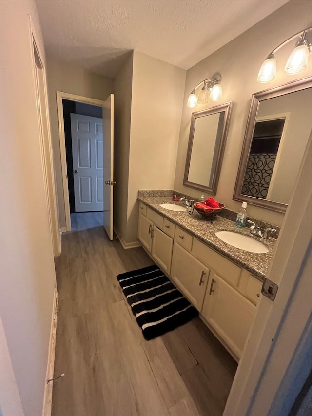 bathroom featuring a textured ceiling, double vanity, wood finished floors, and a sink