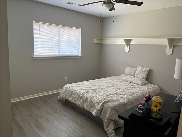 bedroom featuring visible vents, baseboards, wood finished floors, a textured ceiling, and a ceiling fan