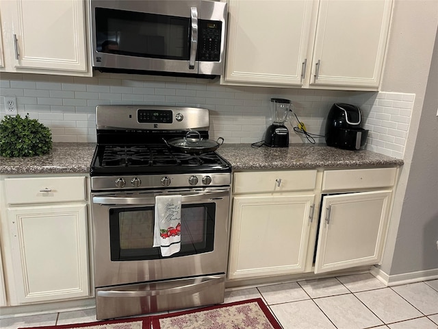 kitchen featuring tasteful backsplash, stone counters, stainless steel appliances, light tile patterned flooring, and white cabinetry