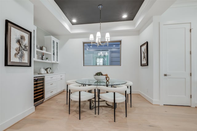 dining room featuring baseboards, wine cooler, a chandelier, light wood-style flooring, and a raised ceiling