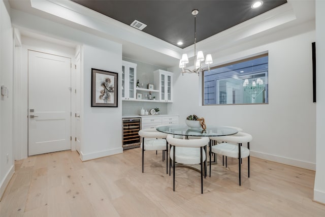 dining room with visible vents, beverage cooler, light wood-type flooring, a tray ceiling, and an inviting chandelier