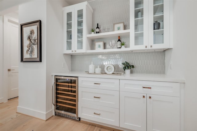 bar with backsplash, baseboards, beverage cooler, a dry bar, and light wood-style floors