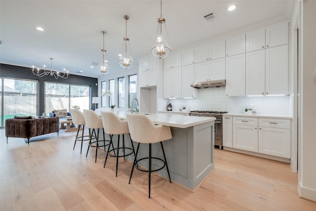 kitchen with an inviting chandelier, light countertops, under cabinet range hood, high end stainless steel range oven, and backsplash