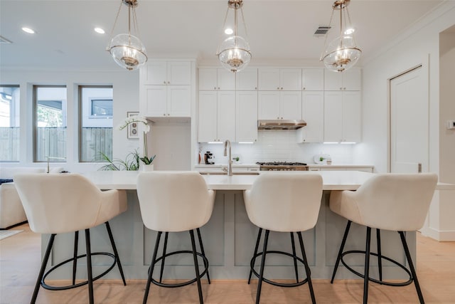 kitchen featuring light wood finished floors, light countertops, under cabinet range hood, crown molding, and tasteful backsplash