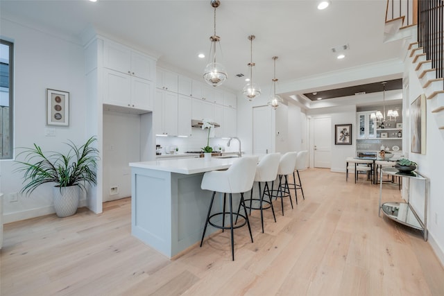 kitchen featuring light wood-type flooring, a kitchen bar, ornamental molding, white cabinetry, and decorative backsplash