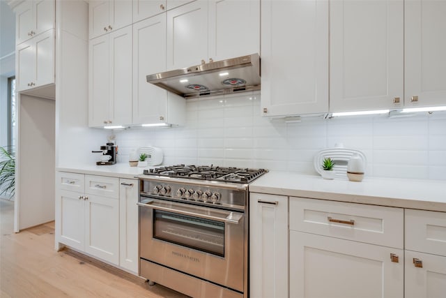 kitchen with decorative backsplash, stainless steel stove, light countertops, and under cabinet range hood