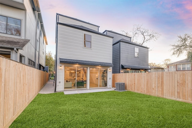 rear view of property featuring a yard, central AC, and a fenced backyard