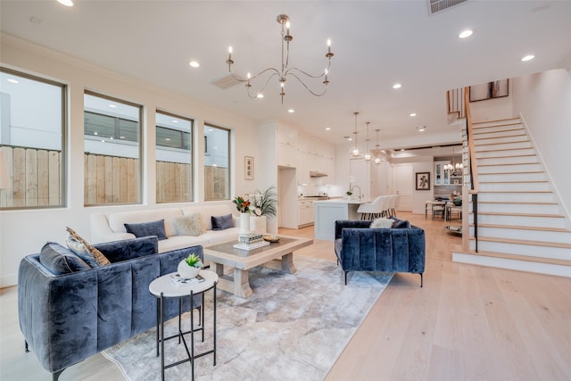 living area featuring recessed lighting, light wood-type flooring, an inviting chandelier, and stairs