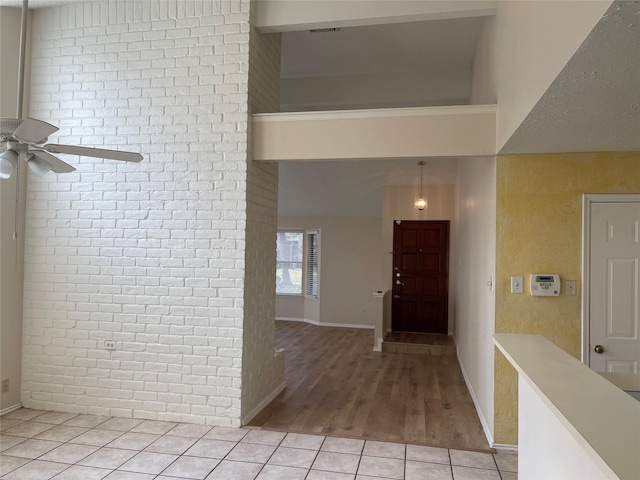 foyer with light tile patterned floors, brick wall, a towering ceiling, and a ceiling fan