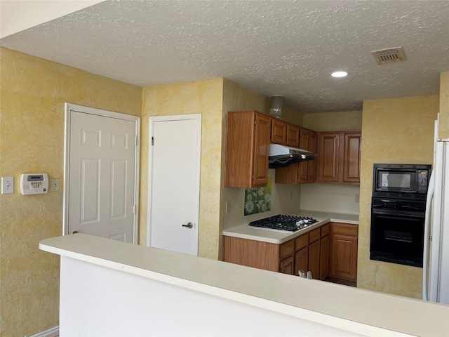 kitchen with black appliances, light countertops, under cabinet range hood, a textured ceiling, and a textured wall