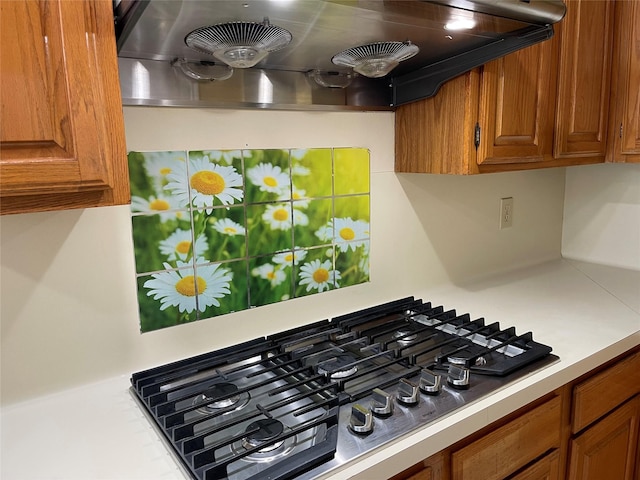 details with light countertops, stainless steel gas stovetop, brown cabinets, and ventilation hood