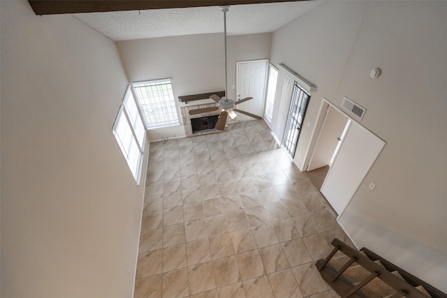 foyer entrance featuring visible vents, ceiling fan, high vaulted ceiling, a fireplace, and a textured ceiling