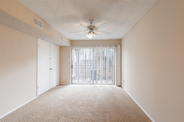 empty room with carpet flooring, a textured ceiling, visible vents, and a ceiling fan