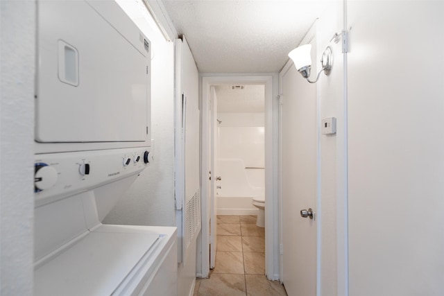 washroom with light tile patterned flooring, laundry area, a textured ceiling, and stacked washer / drying machine