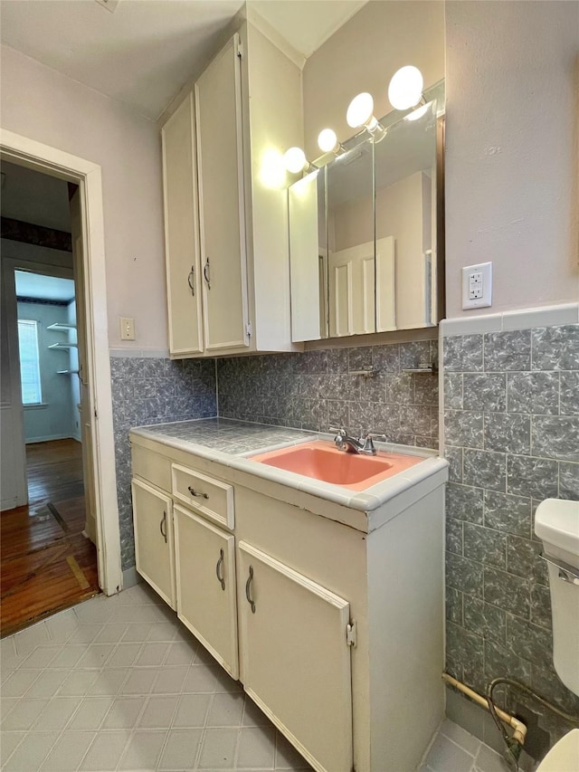 half bath with wainscoting, tile walls, vanity, and toilet