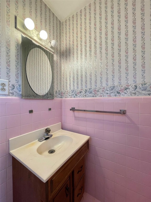 bathroom with wallpapered walls, tile walls, vanity, and wainscoting