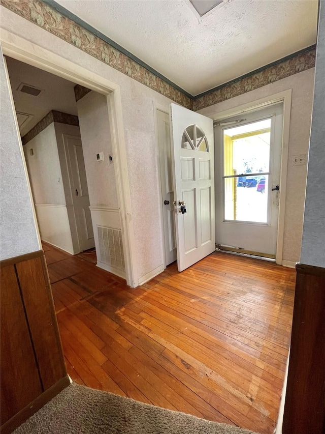 entrance foyer with light wood-style flooring, visible vents, and a textured ceiling