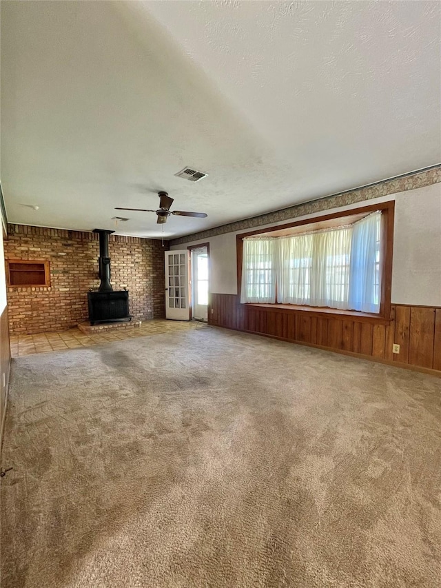 unfurnished living room with visible vents, carpet, a wainscoted wall, and a wood stove