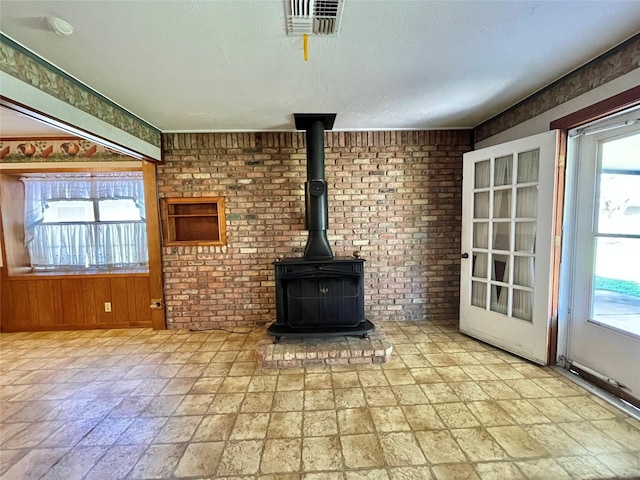 unfurnished living room featuring a wood stove, plenty of natural light, visible vents, and brick wall