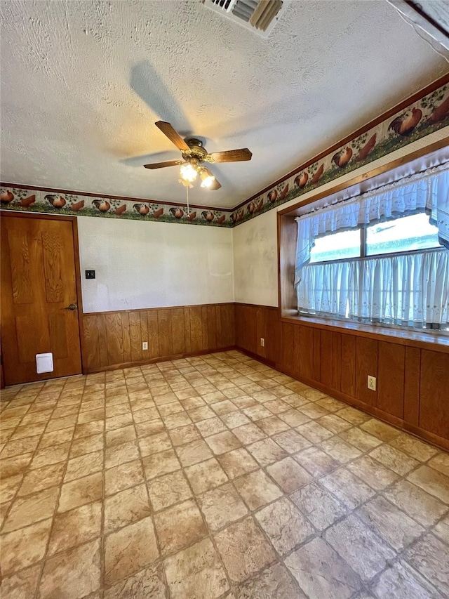 empty room featuring visible vents, a textured ceiling, ceiling fan, and a wainscoted wall