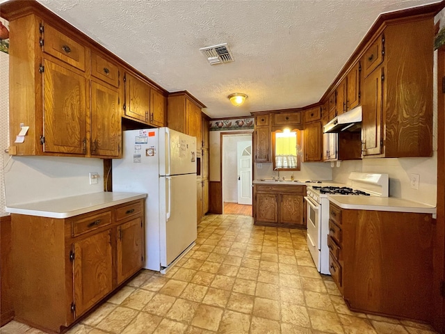 kitchen featuring visible vents, under cabinet range hood, light countertops, brown cabinetry, and white appliances