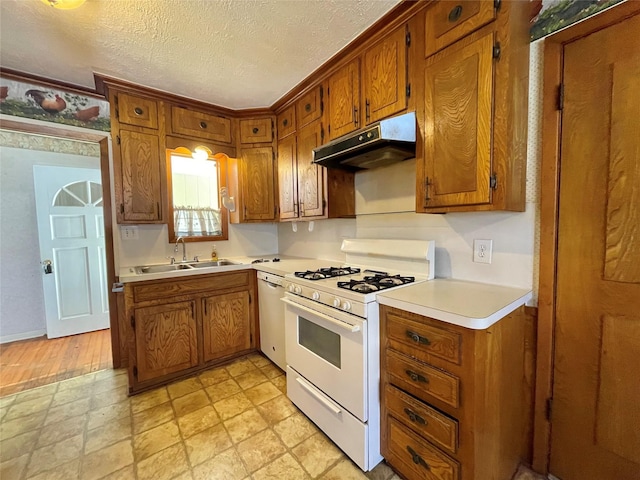 kitchen with brown cabinets, under cabinet range hood, a sink, a textured ceiling, and white appliances