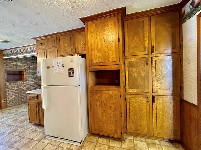 kitchen with visible vents, brown cabinets, a textured ceiling, and freestanding refrigerator