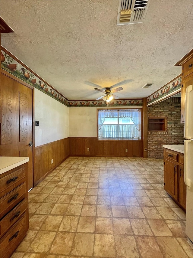 empty room with wooden walls, a ceiling fan, visible vents, and wainscoting