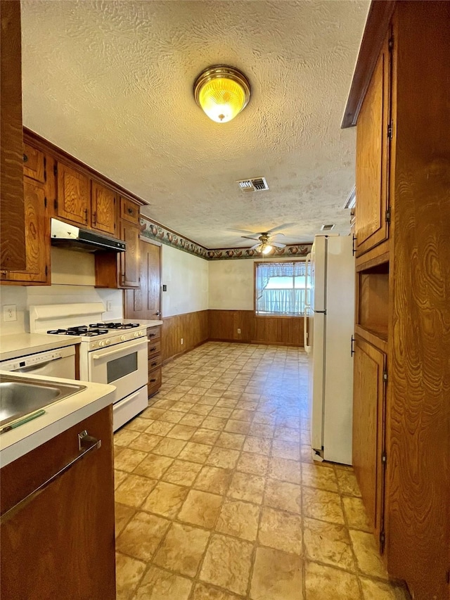 kitchen with visible vents, under cabinet range hood, wainscoting, white appliances, and a ceiling fan