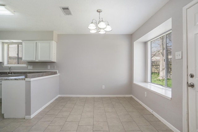 kitchen with visible vents, a sink, white cabinetry, baseboards, and a chandelier