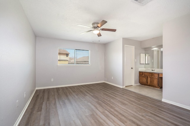 unfurnished bedroom with light wood-type flooring, visible vents, a sink, a textured ceiling, and baseboards