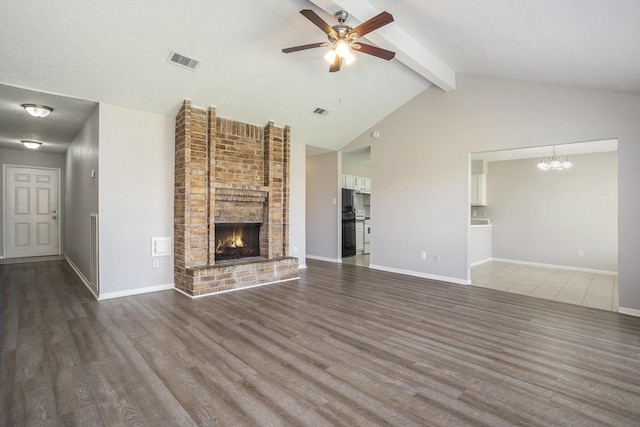 unfurnished living room featuring visible vents, ceiling fan with notable chandelier, lofted ceiling with beams, wood finished floors, and a brick fireplace