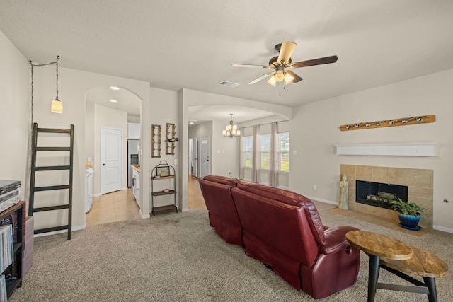 living area featuring visible vents, a tiled fireplace, ceiling fan with notable chandelier, arched walkways, and light colored carpet