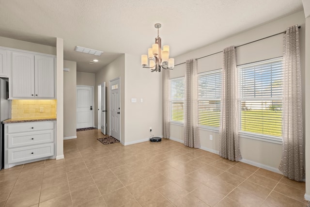 unfurnished dining area featuring light tile patterned floors, baseboards, visible vents, an inviting chandelier, and a textured ceiling