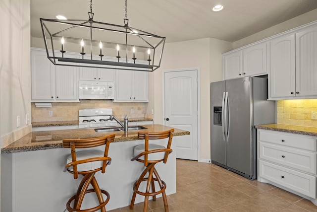 kitchen featuring white appliances, dark stone counters, a kitchen breakfast bar, and a sink