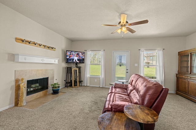 living area featuring a ceiling fan, carpet, baseboards, a textured ceiling, and a tiled fireplace